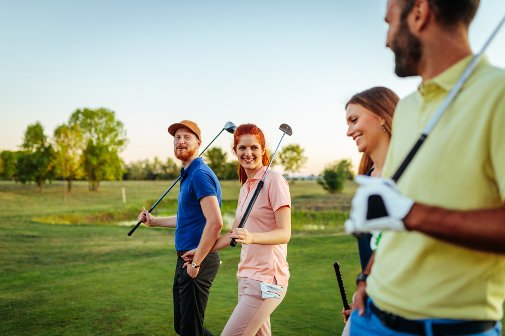 A group of four friends walking and talking up to their next shot on a golf course with clubs in their hands. - Ted Britt Chevrolet Sterling, VA