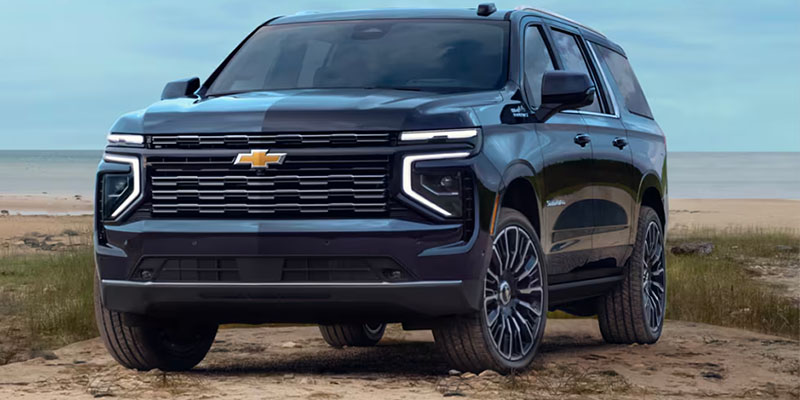 All-new black 2025 Chevy Suburban parked in front of a body of water on the sand. - Ted Britt Chevrolet Sterling, VA